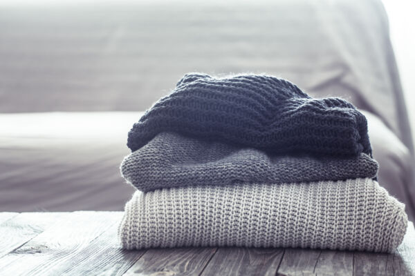 What To Wear With A Knitted Sweater.A stack of knitted sweaters on a wooden table, in the interior of the living room. The concept of autumn comfort